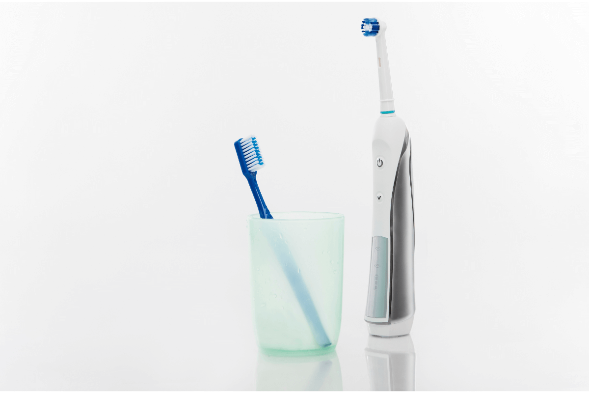 Klasický zubní kartáček ve skleničce a stojící elektrický zubní kartáček
